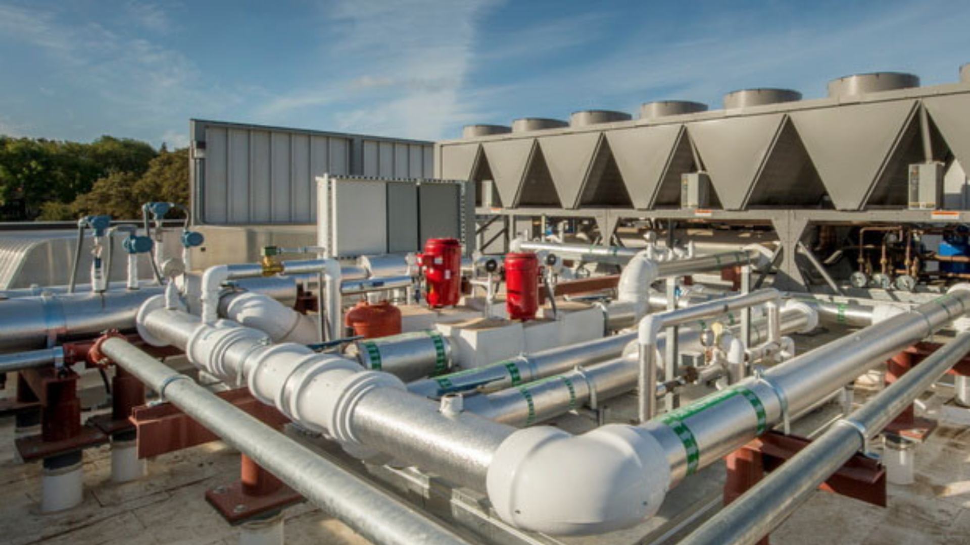 Industrial HVAC system with large pipes, valves, and cooling units on a rooftop under a clear sky. Industrial HVAC system with large pipes, valves, and cooling units on a rooftop under a clear sky.